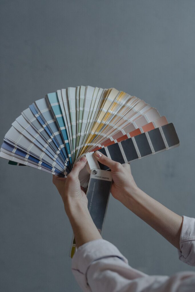 Hands holding color swatch samples in a fan shape against a gray background.