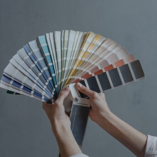Hands holding color swatch samples in a fan shape against a gray background.