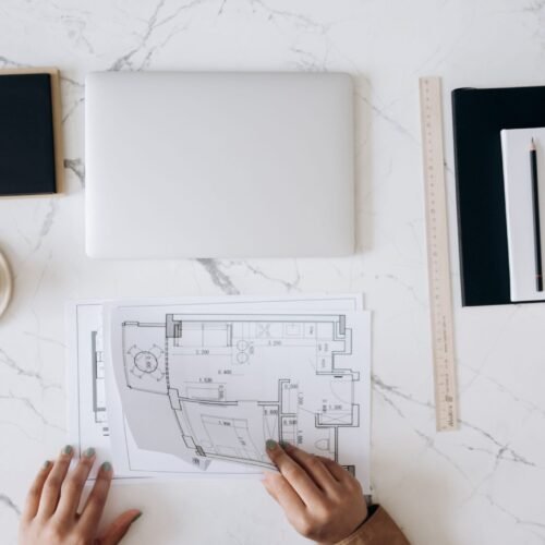 Top view of an architect's desk featuring blueprints, laptop, notebook, and coffee cup on a marble surface.