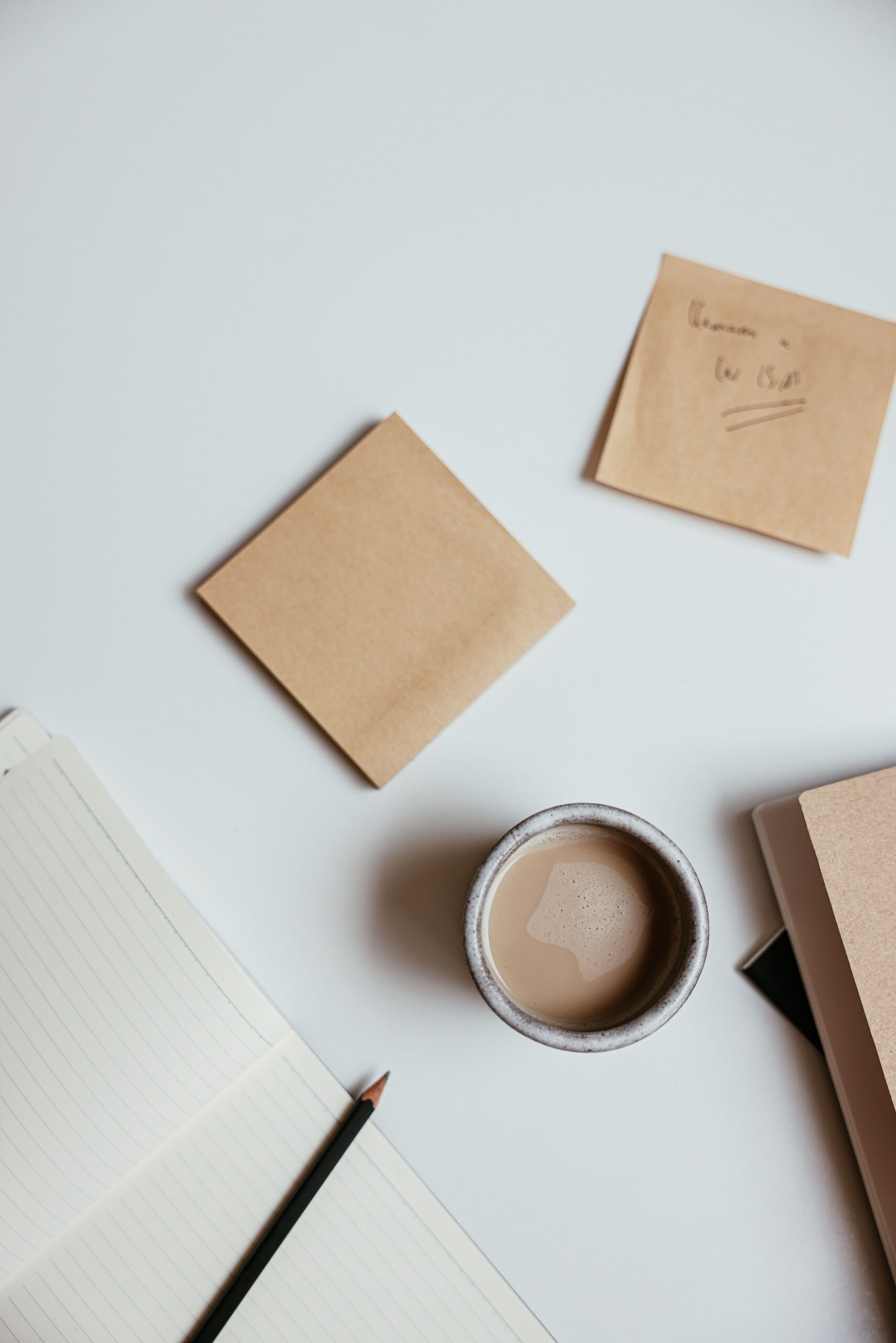 Flat lay of a minimalist workspace with coffee, notebooks, and sticky notes on a clean table.
